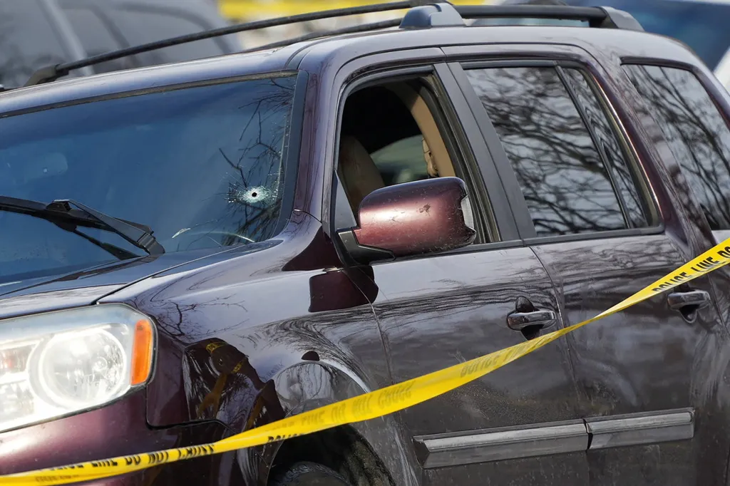 A bullet hole in the windshield of a car behind police tape.