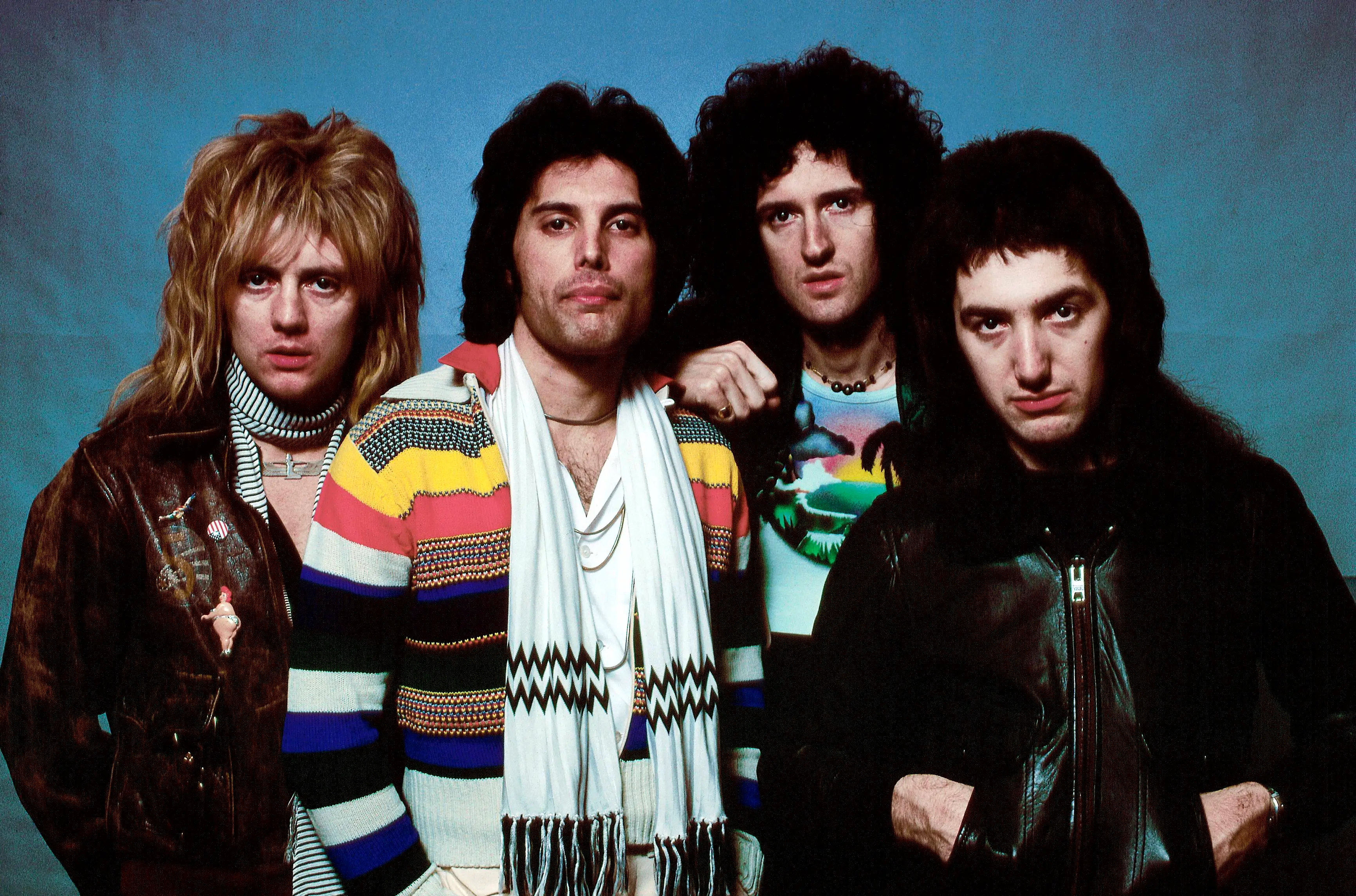 Posed studio portrait of the rock band Queen, featuring Roger Taylor, Freddie Mercury, Brian May, and John Deacon.