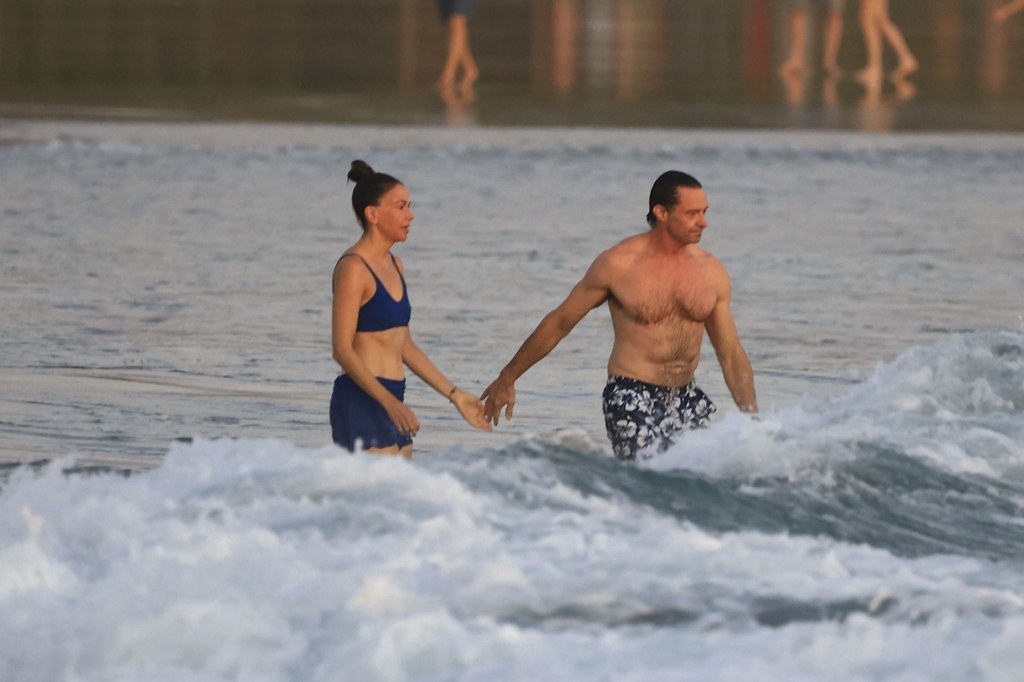 Hugh Jackman and Sutton Foster hold hands while wading in the ocean.