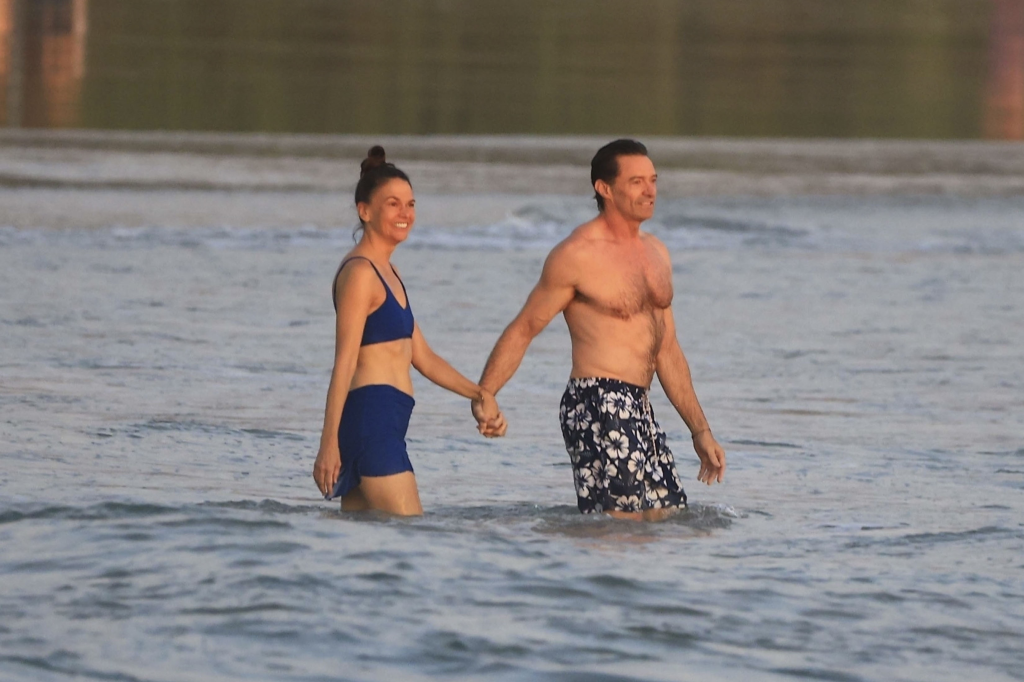 Hugh Jackman and Sutton Foster hold hands while wading in the ocean.