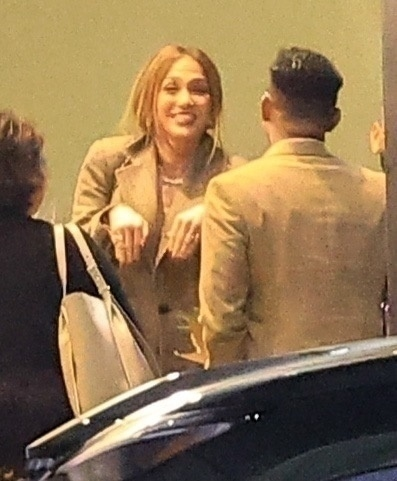 Jennifer Lopez smiling while talking to someone, with Samuel Affleck standing near her.