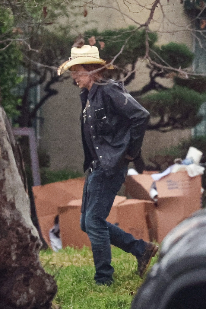 Mickey Rourke walking outdoors while wearing a cowboy hat, dark jacket, and jeans.