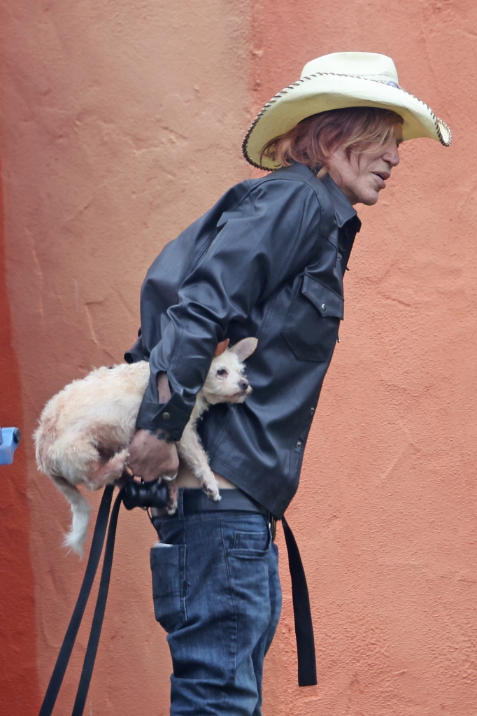 Mickey Rourke holding a small dog under his arm.