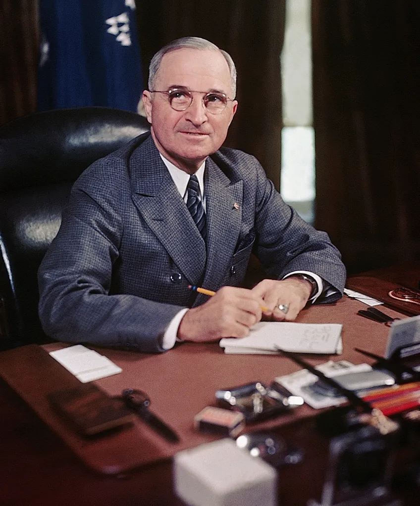 President Harry S. Truman seated at his desk holding a pencil.