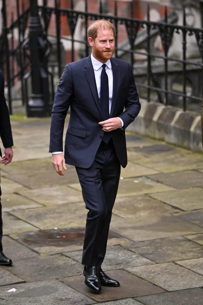 Prince Harry, Duke of Sussex, in a dark suit and tie, smiling and walking towards the camera.