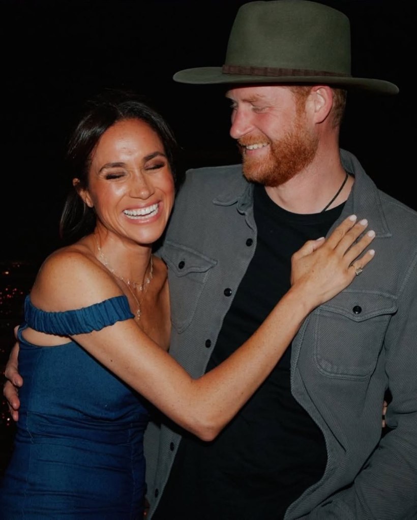 Meghan Markle laughing with her eyes closed, embracing Prince Harry, who is wearing a hat.