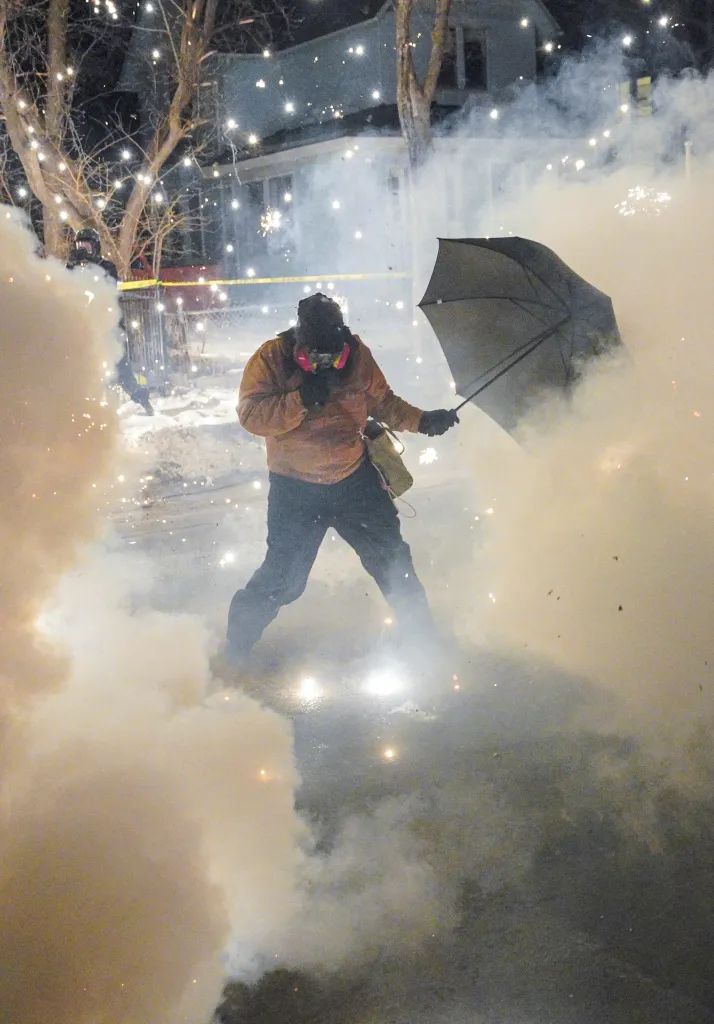 A protester holds an umbrella as fireworks and pepper balls go off during a wild demonstration.