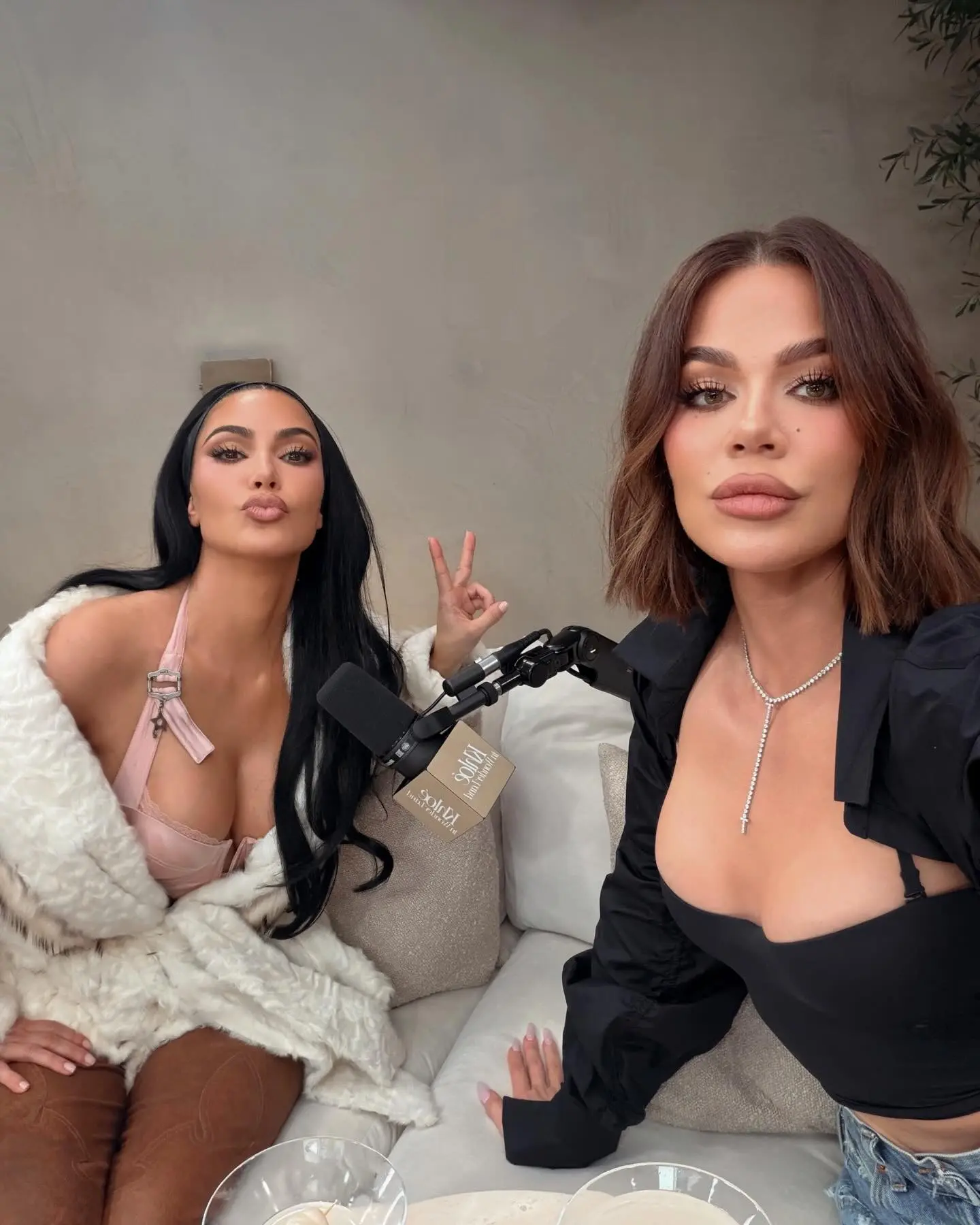 Kim and Khloé Kardashian posing for a photo during a podcast recording.
