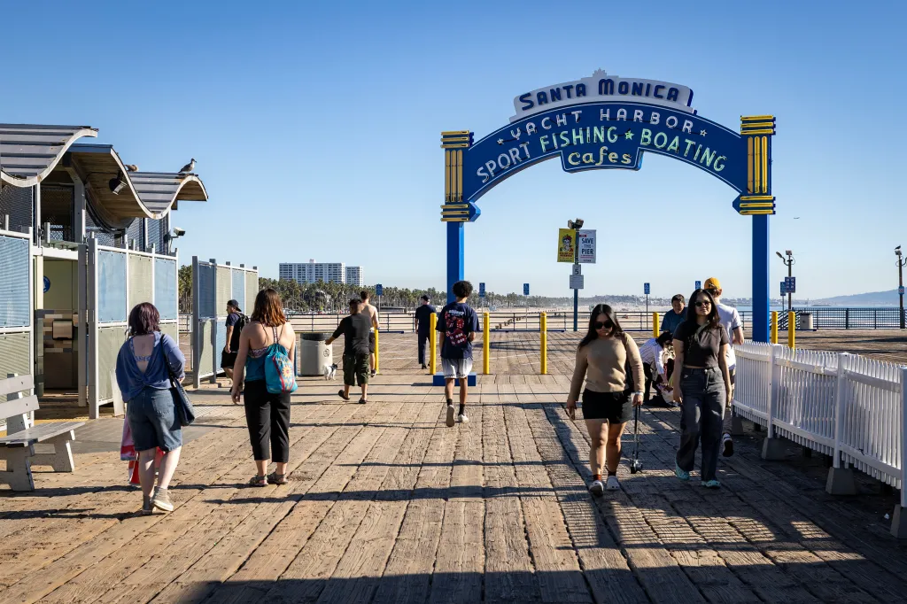 People walking on the Santa Monica Pier boardwalk under an archway sign that reads 
