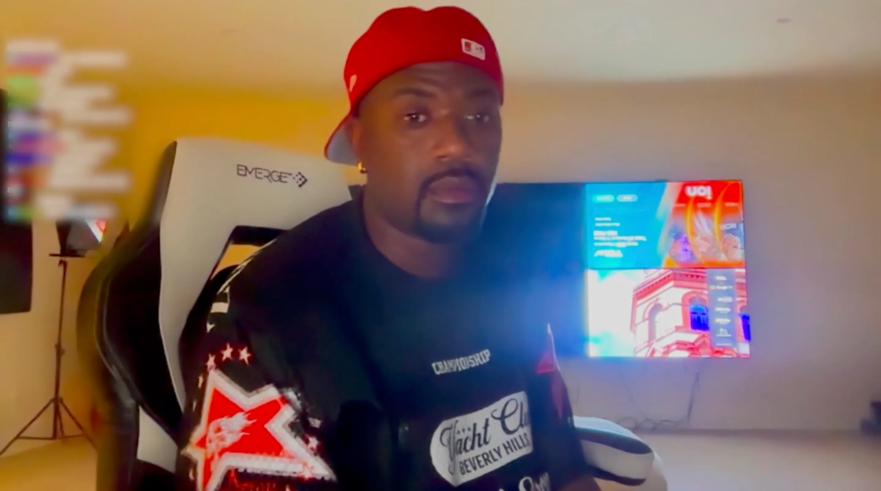 Ray J sitting in an Emerge gaming chair, wearing a red hat and black t-shirt.