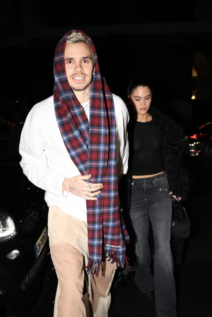 Romeo Beckham with a red and blue plaid scarf over his head, next to Kim Turnbull in a black crop top and wide-leg pants.