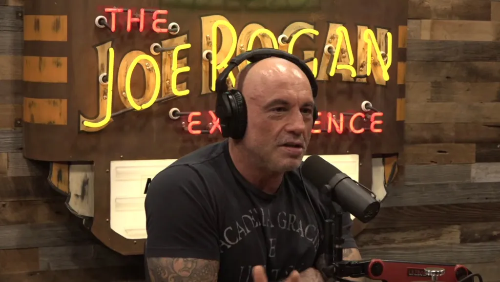 Joe Rogan wearing headphones and speaking into a microphone.
