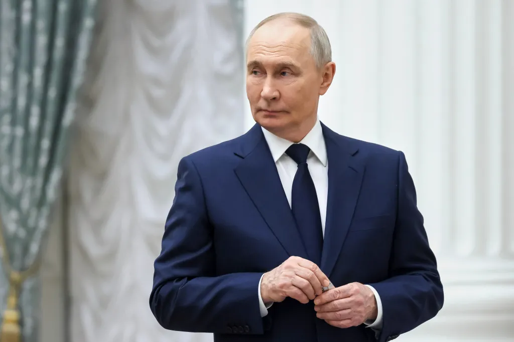 Russian President Vladimir Putin in a navy suit, white shirt, and dark tie, looking left.