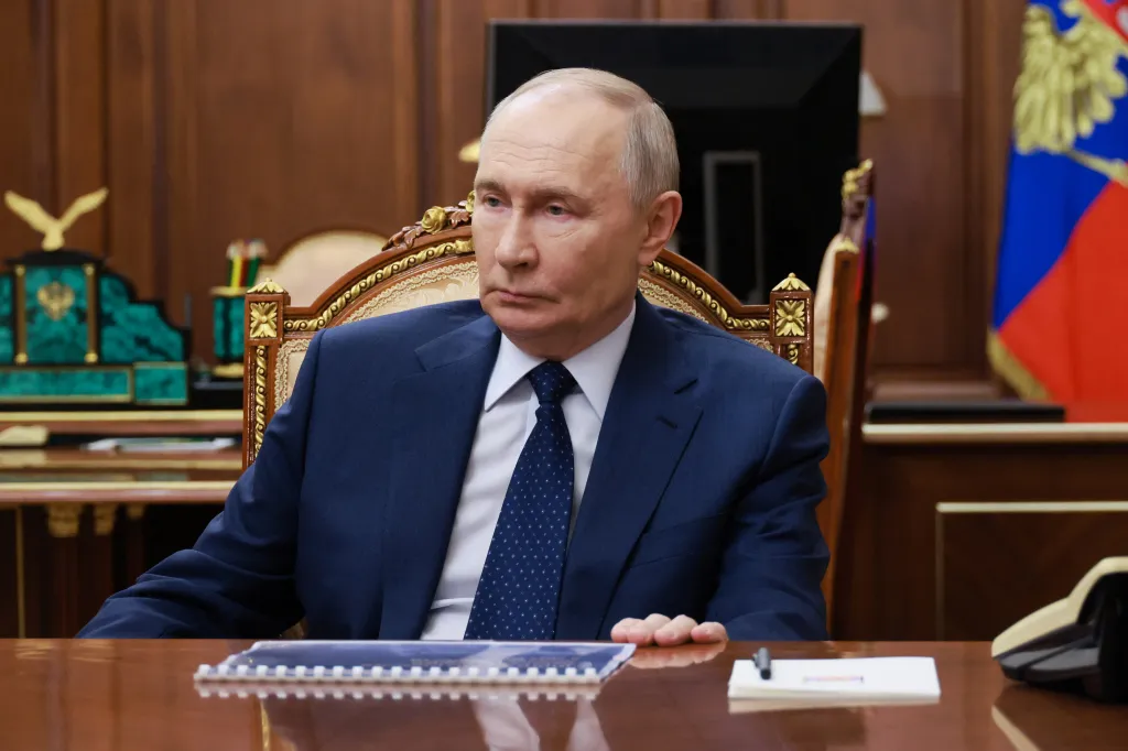 Russian President Vladimir Putin in a suit and tie sitting at a large wooden desk.
