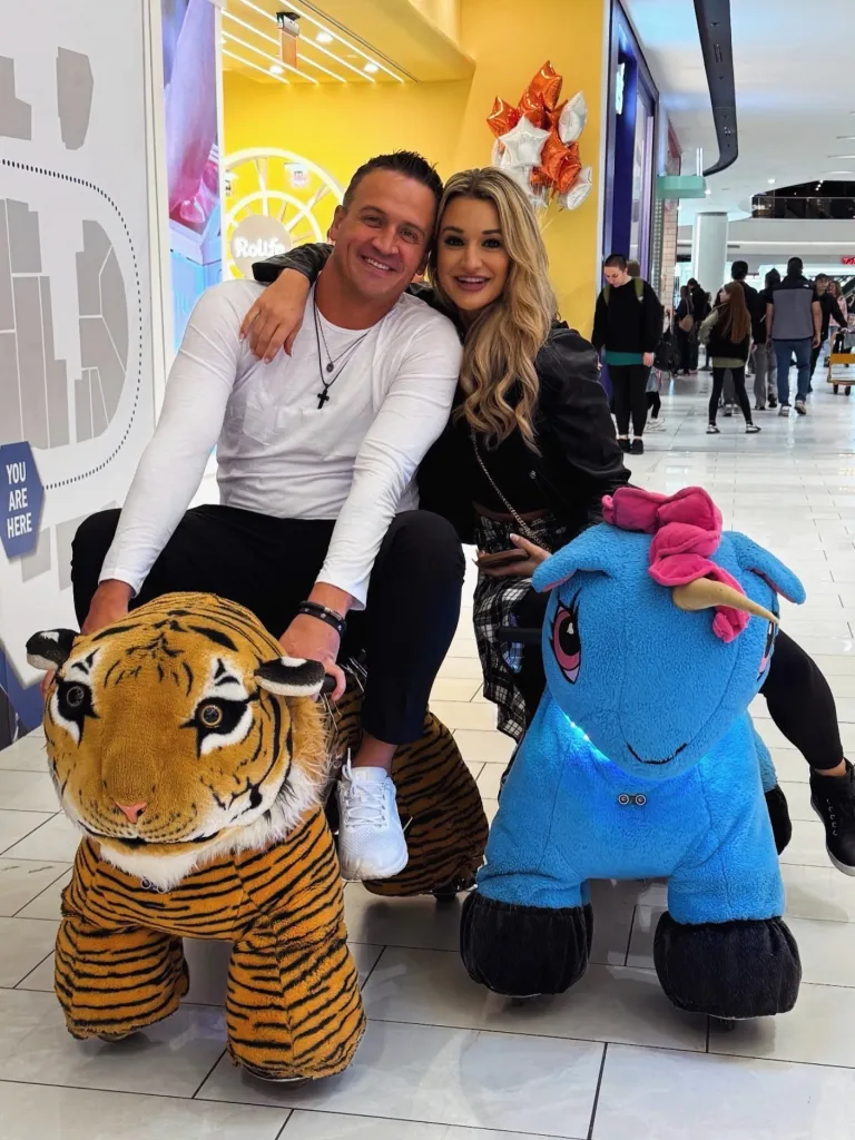 Ryan Lochte and his new girlfriend pose on animal-shaped rides in a mall.