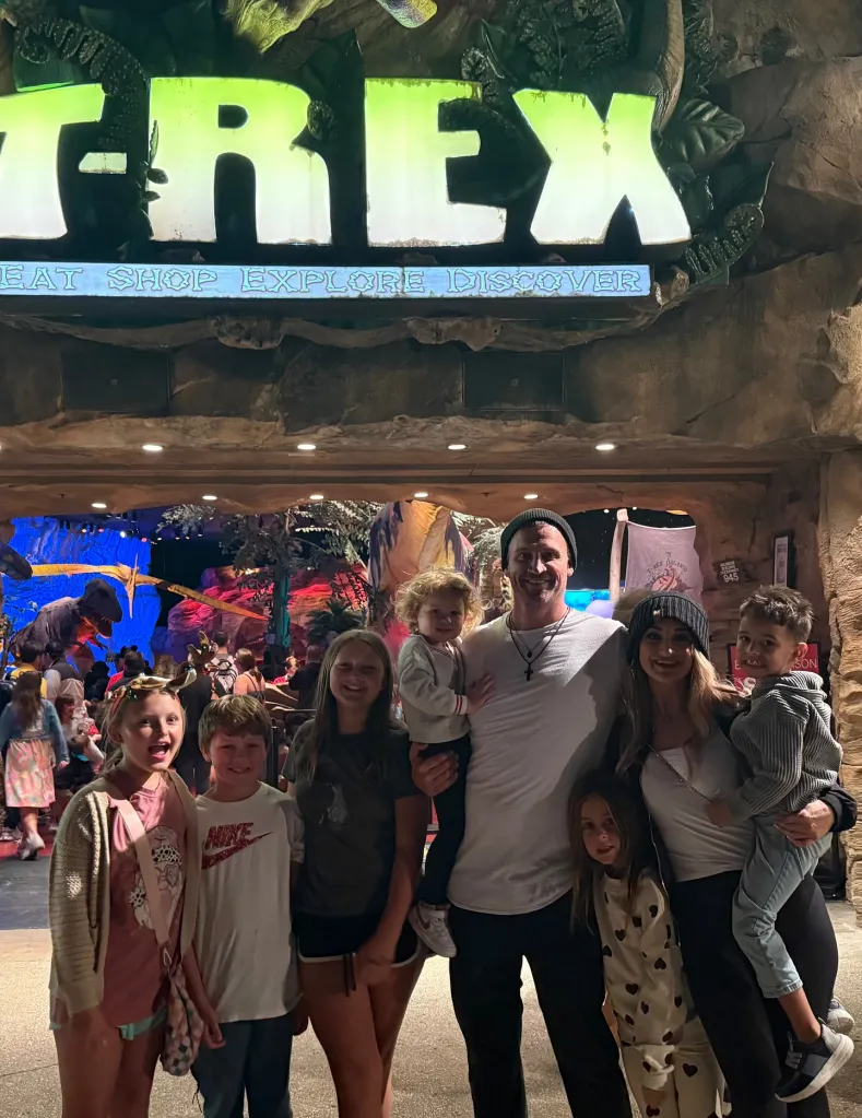 Ryan Lochte and his new girlfriend with their six children pose in front of a T-Rex restaurant.