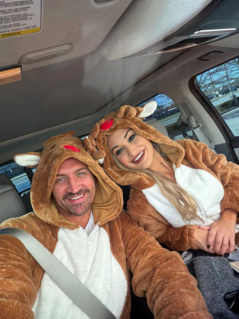 Ryan Lochte and his girlfriend are dressed in reindeer onesies, smiling in a car.