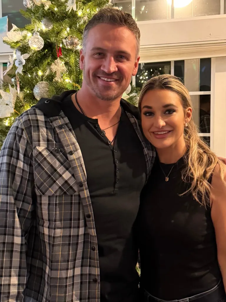 Ryan Lochte and his new girlfriend smiling in front of a Christmas tree.
