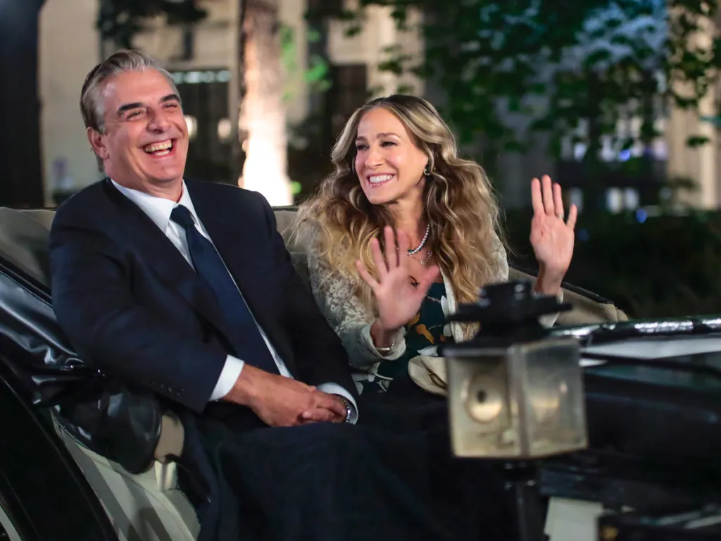 Sarah Jessica Parker and Chris Noth in a carriage, smiling and waving.