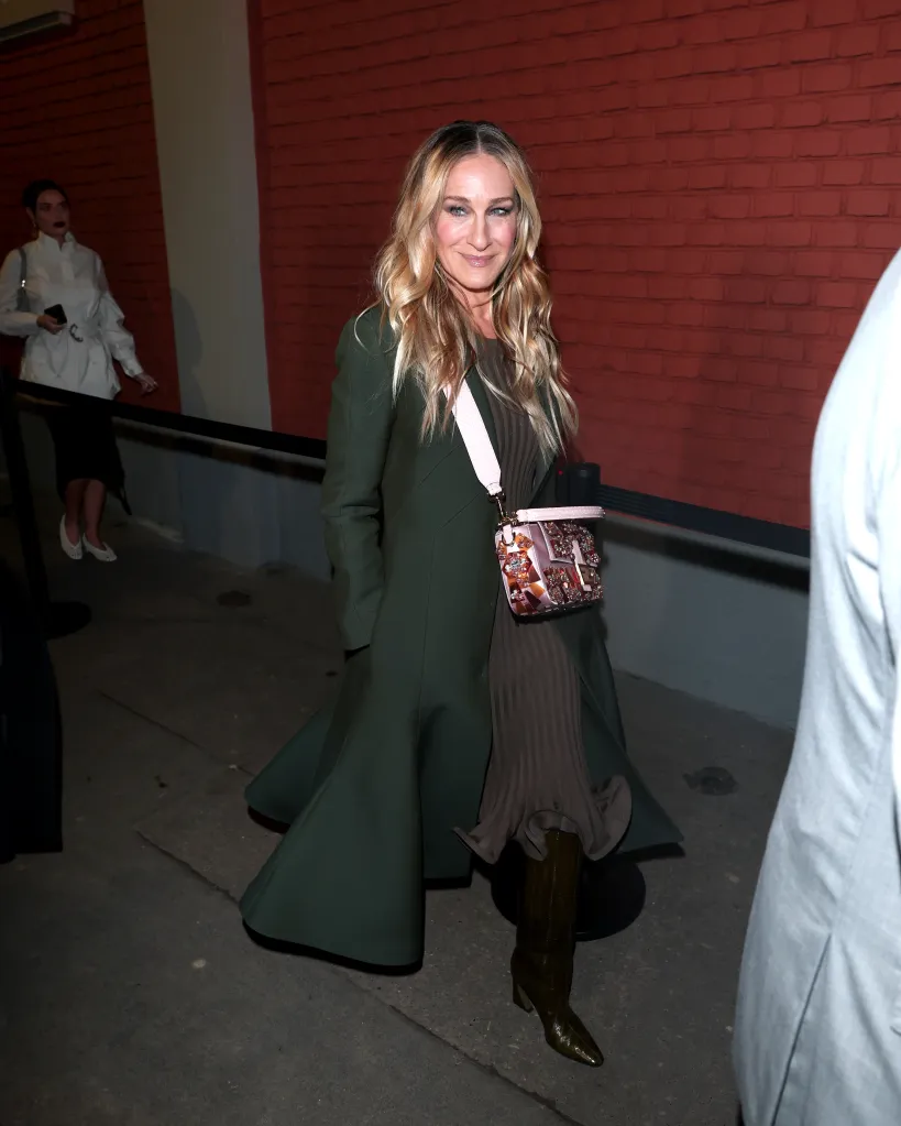 Sarah Jessica Parker arriving at the Fendi fashion show, wearing a dark green coat, a brown pleated dress, and olive green boots, carrying a jeweled pink handbag.