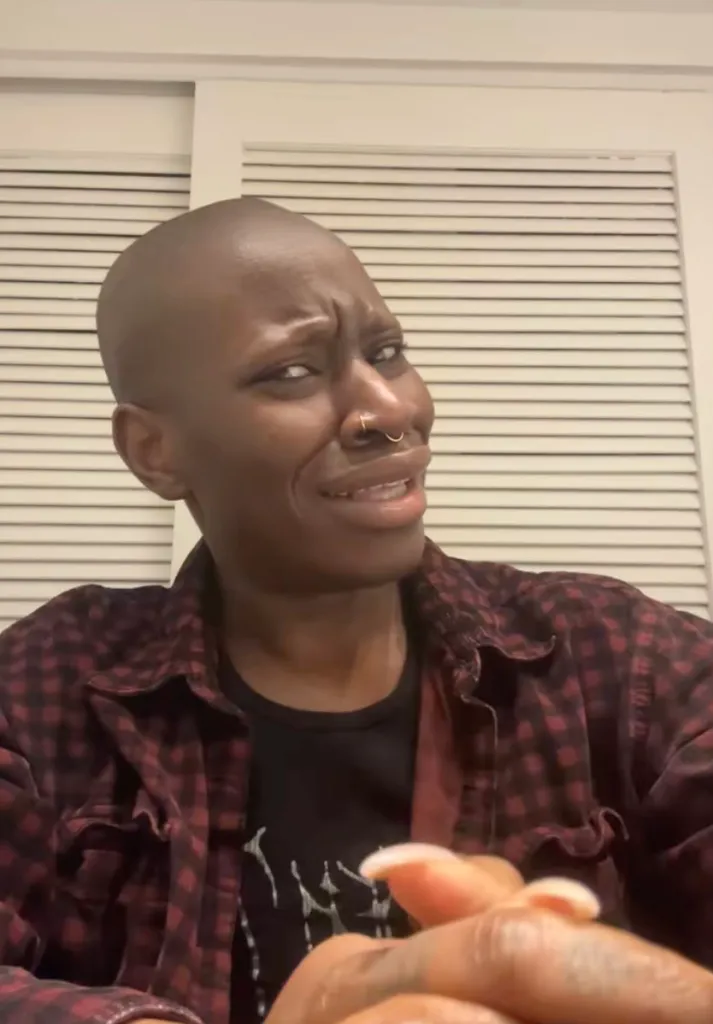 A bald woman with a nose ring making a skeptical face.