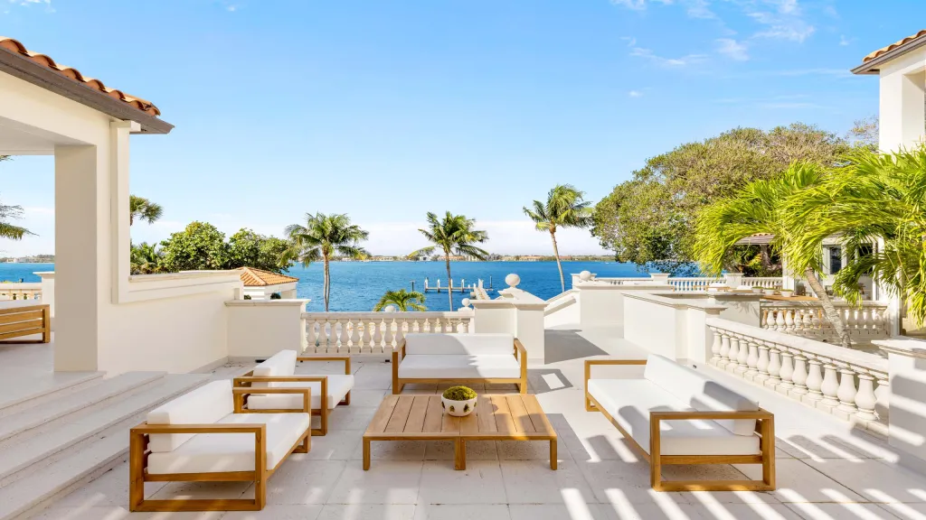 Rooftop observation terrace with white outdoor furniture, a view of palm trees, and the waterfront.