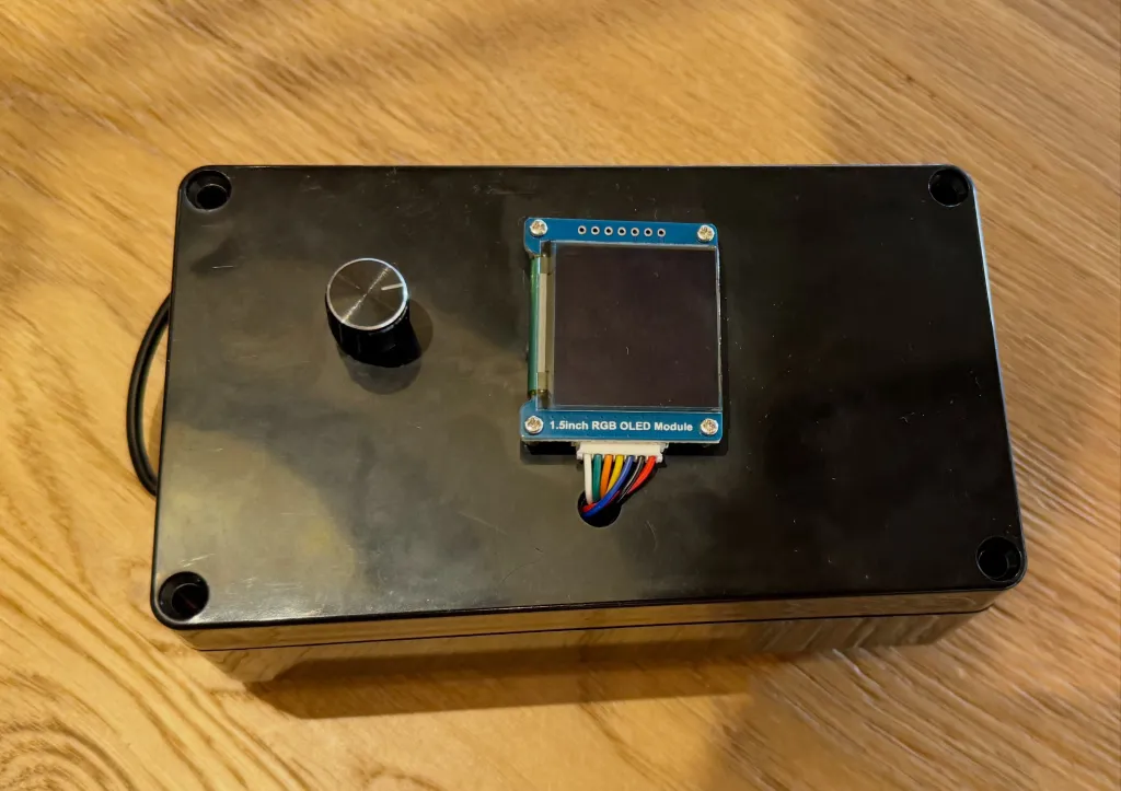 A black rectangular box with a silver knob, a multi-colored wire and a 1.5-inch RGB OLED module.