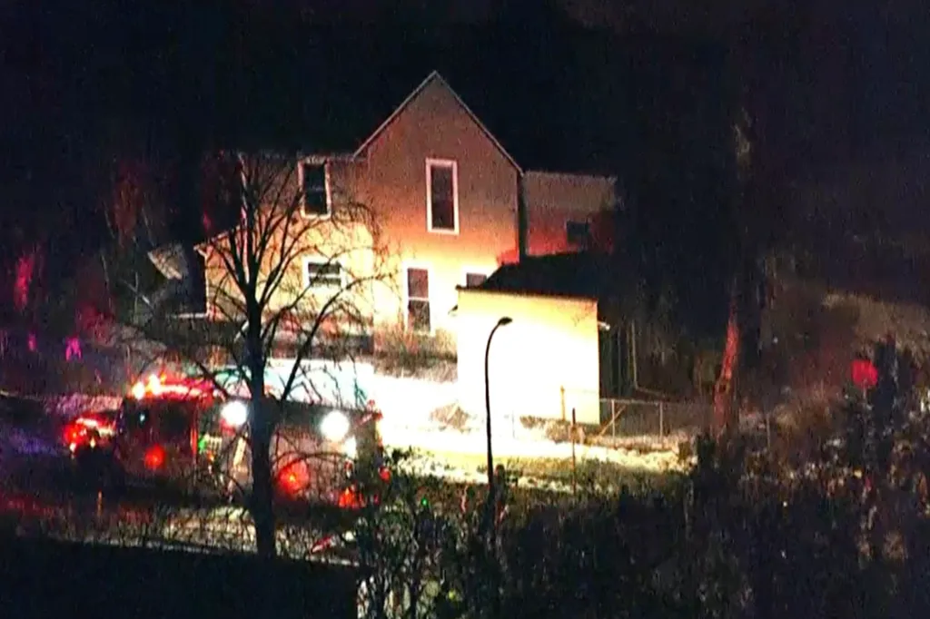 Emergency vehicles with flashing lights outside a house at night.