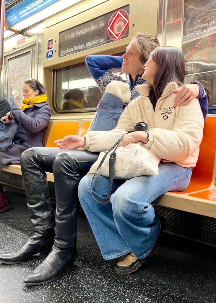 Ansel Elgort and partner on the subway with a baby in a papoose.
