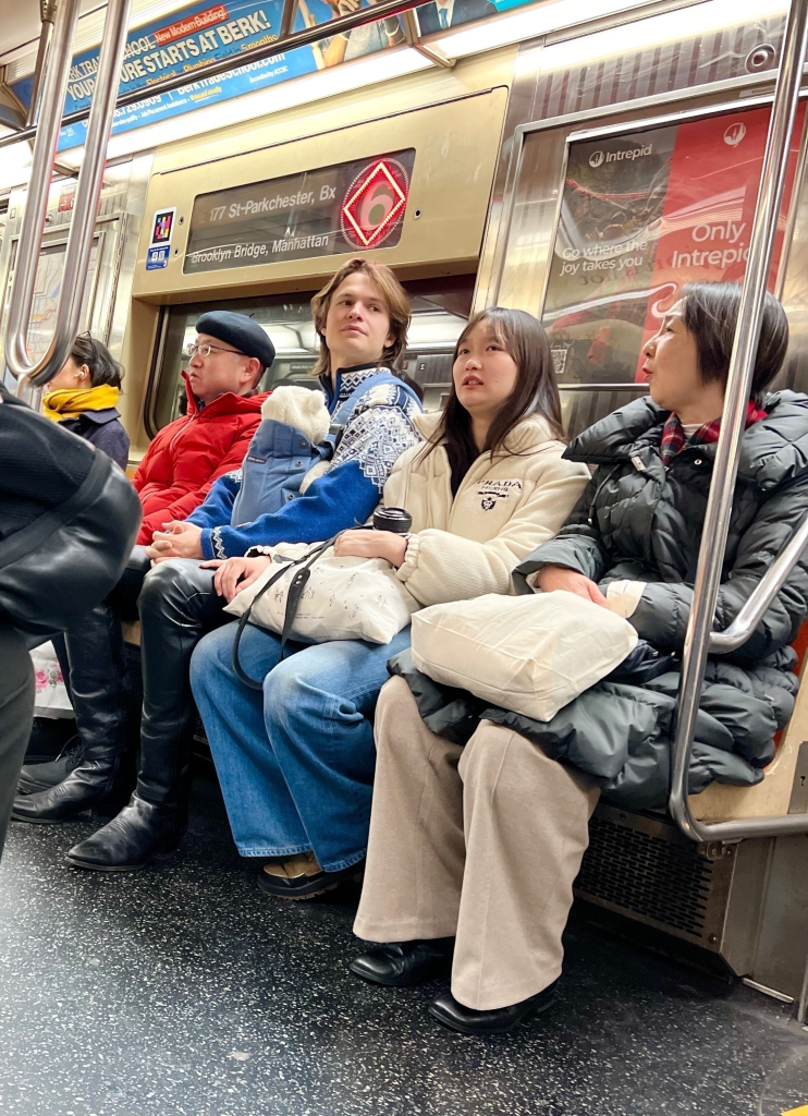 Ansel Elgort, his partner, and her parents riding the New York City subway, with Elgort carrying a baby in a papoose.