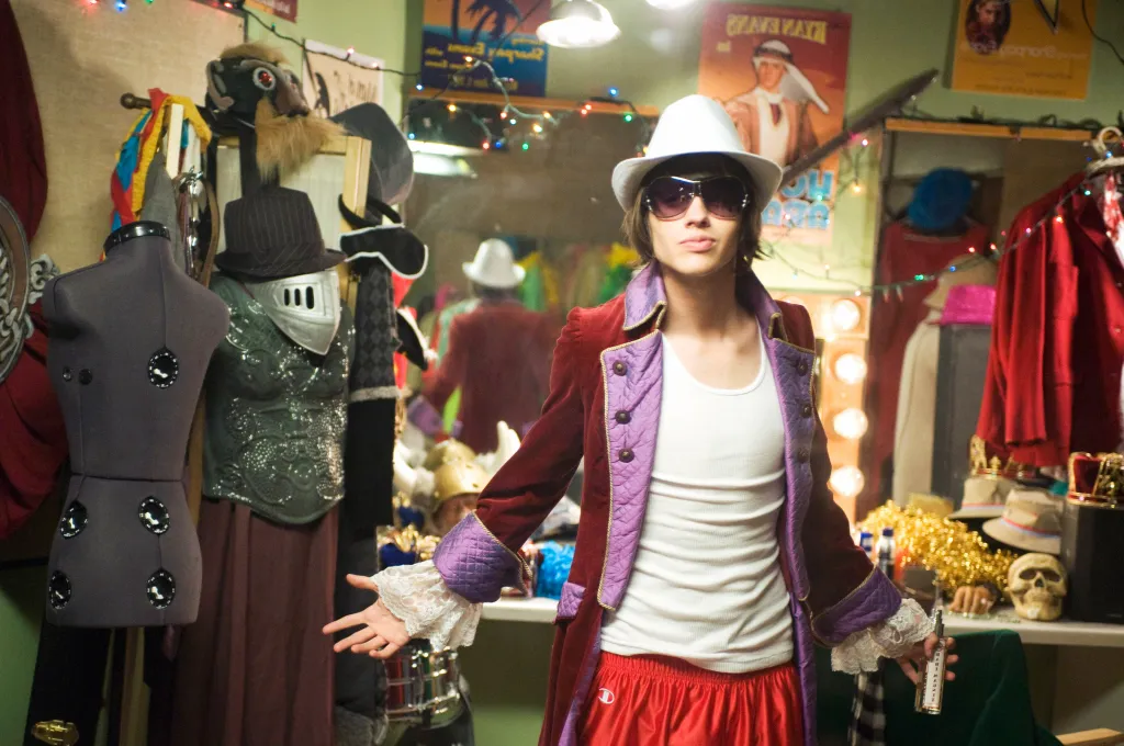 Matt Prokop in a dressing room, wearing a velvet jacket, sunglasses, and a fedora.