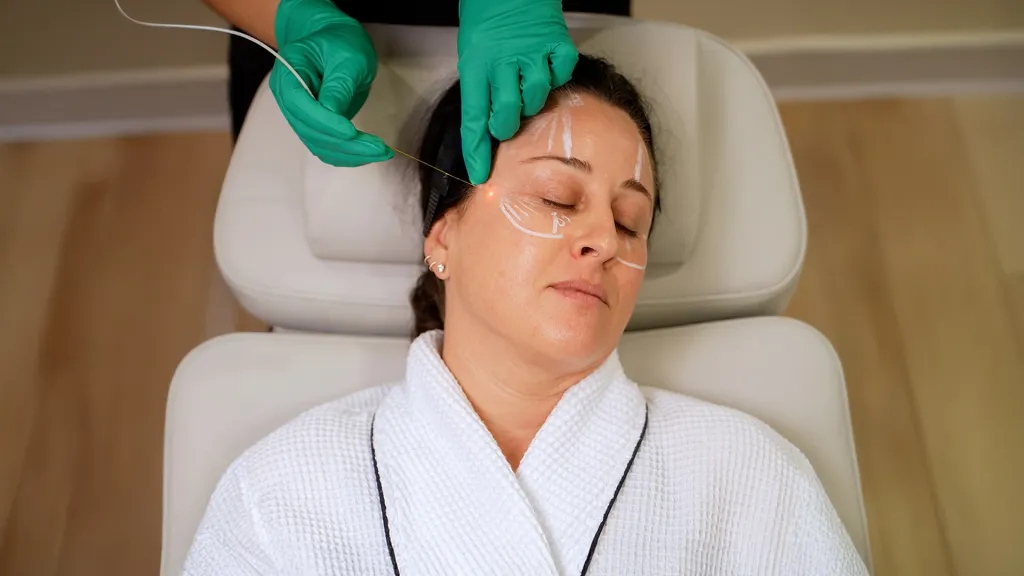 A woman receiving a skin-tightening and fat-melting treatment to her face with a laser