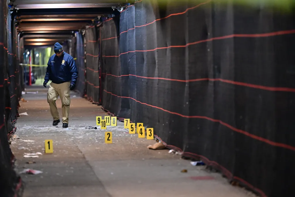 A police officer surveys a crime scene with numbered evidence markers on the ground.