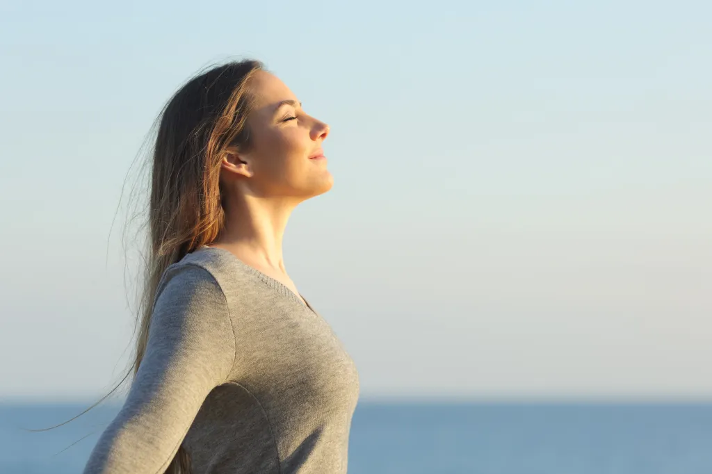 Side profile of a woman with closed eyes smiling, breathing fresh air on the beach.