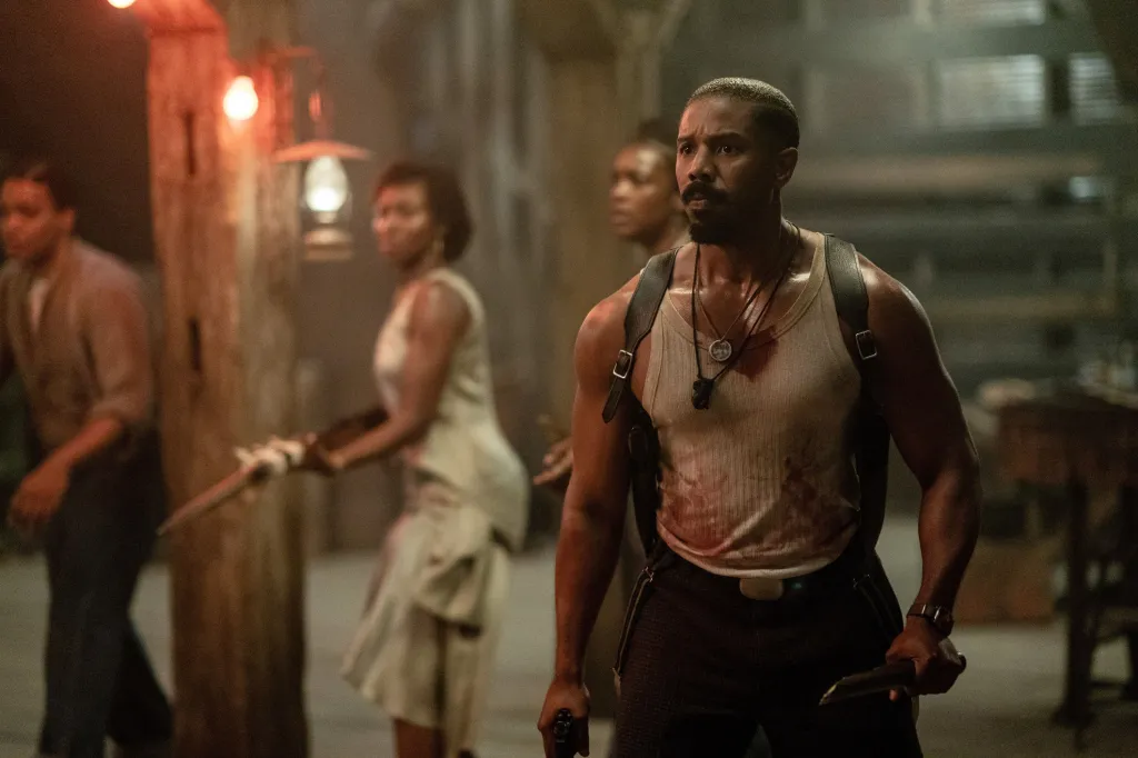 Michael B. Jordan as Smoke, with blood on his tank top and holding a weapon, looking intently forward.