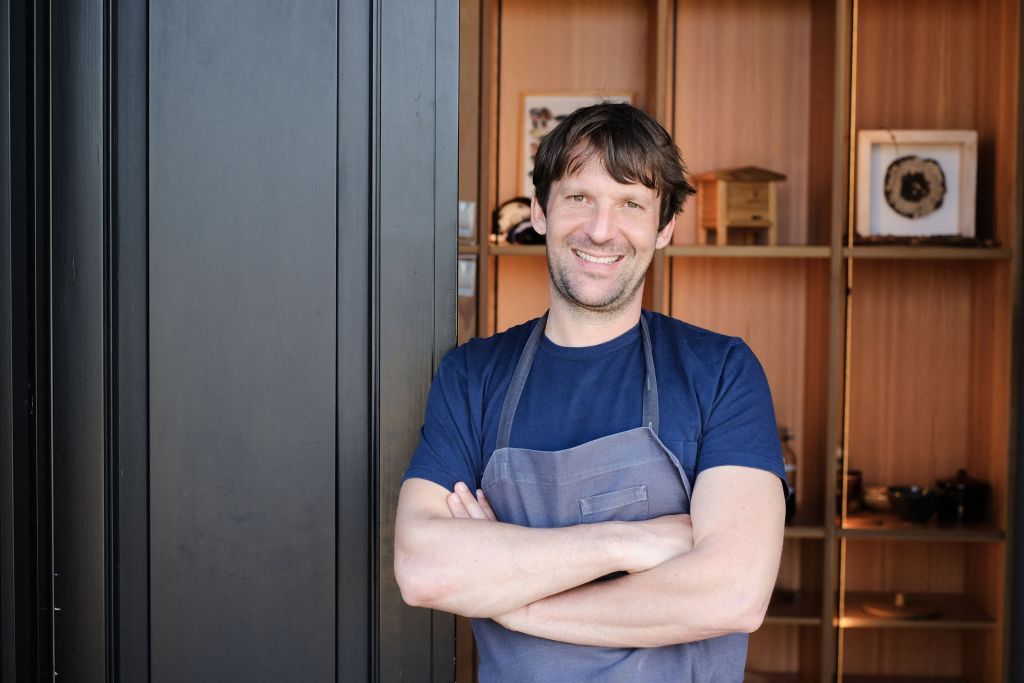 Chef René Redzepi smiling with his arms crossed outside Noma restaurant.