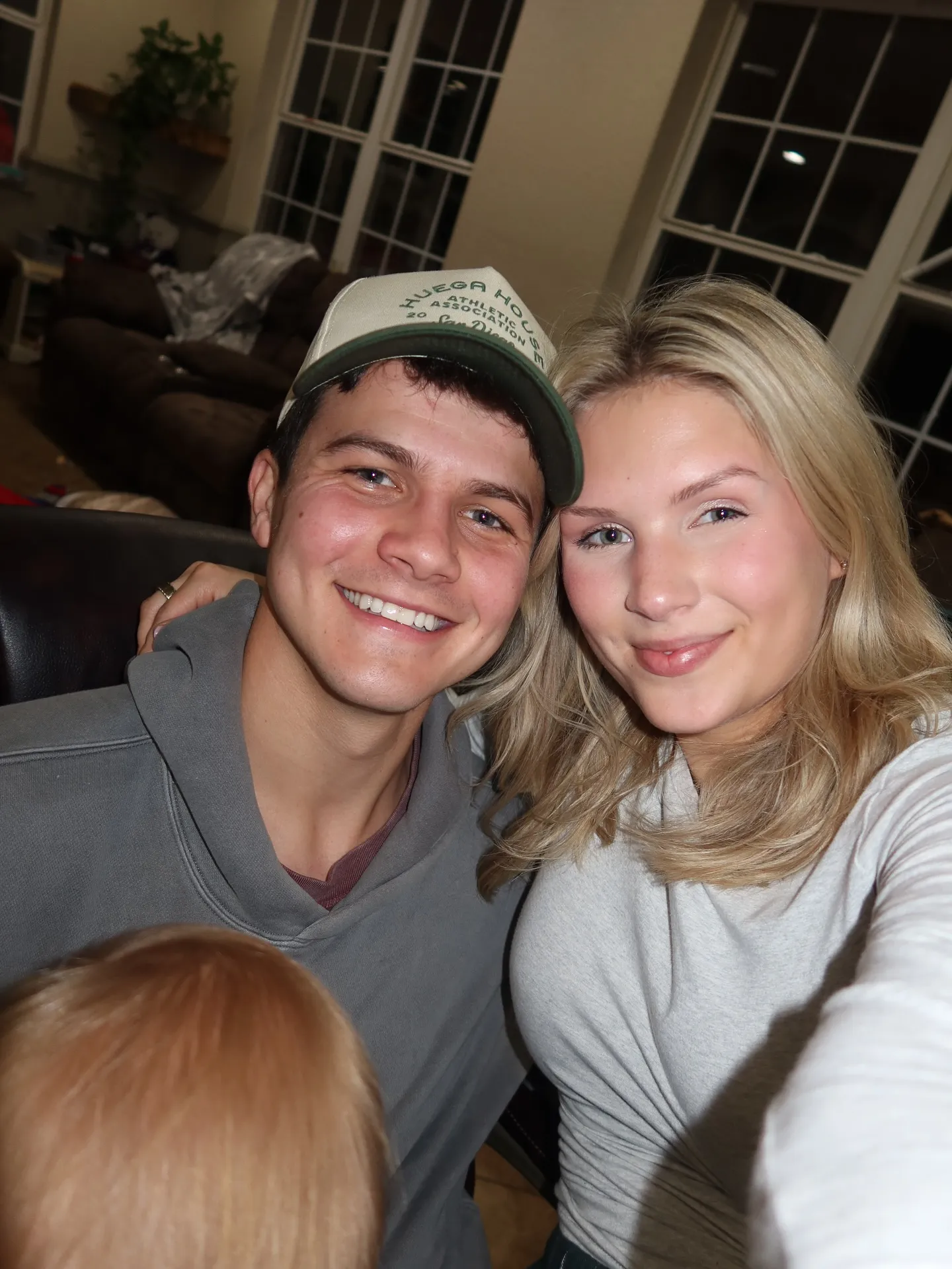 Travis Clark and Katie Bates smiling at the camera, with a baby's head visible in the foreground.