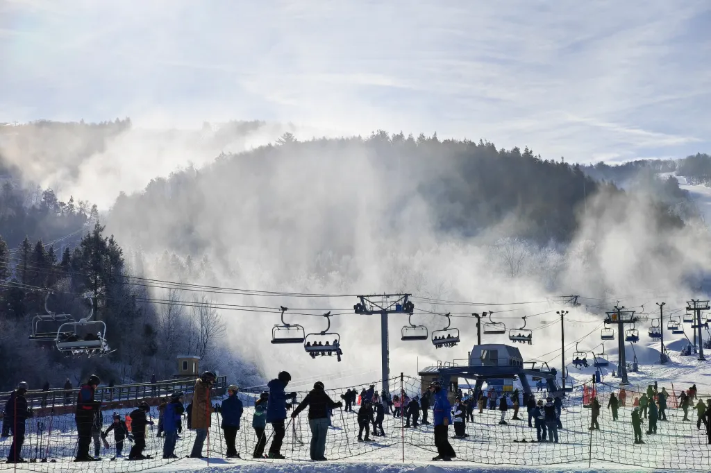 Snowmaking machines creating a mist over the trees at Blue Mountain ski resort with skiers and chairlifts.