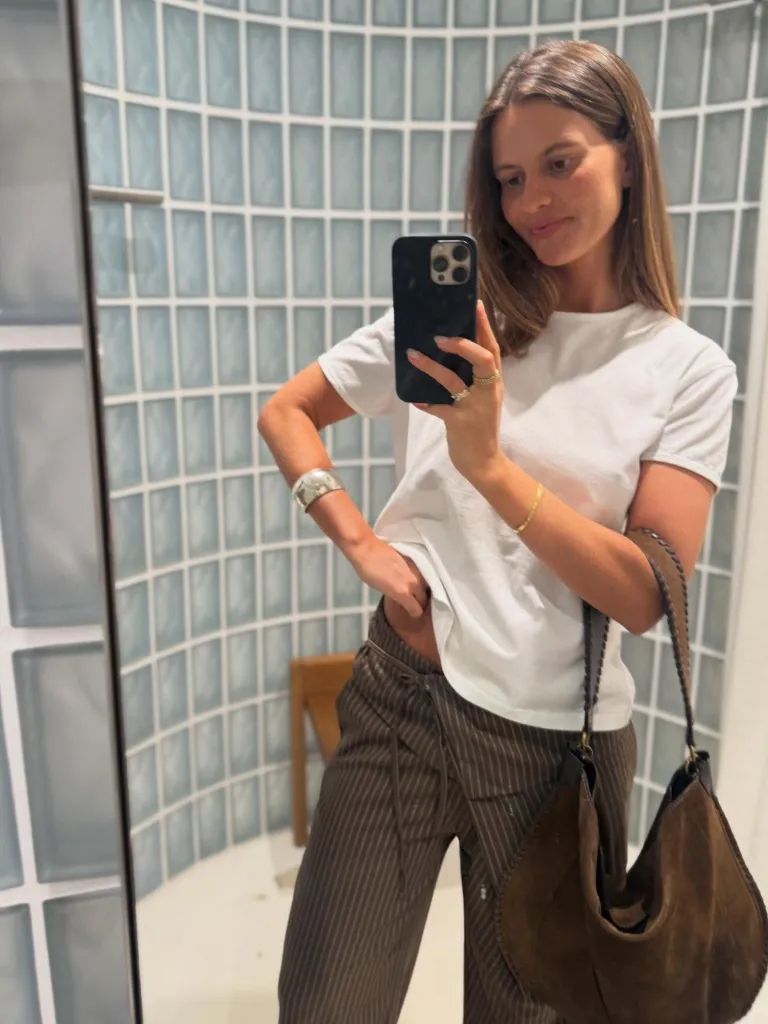 Woman in white t-shirt and striped pants taking a mirror selfie.