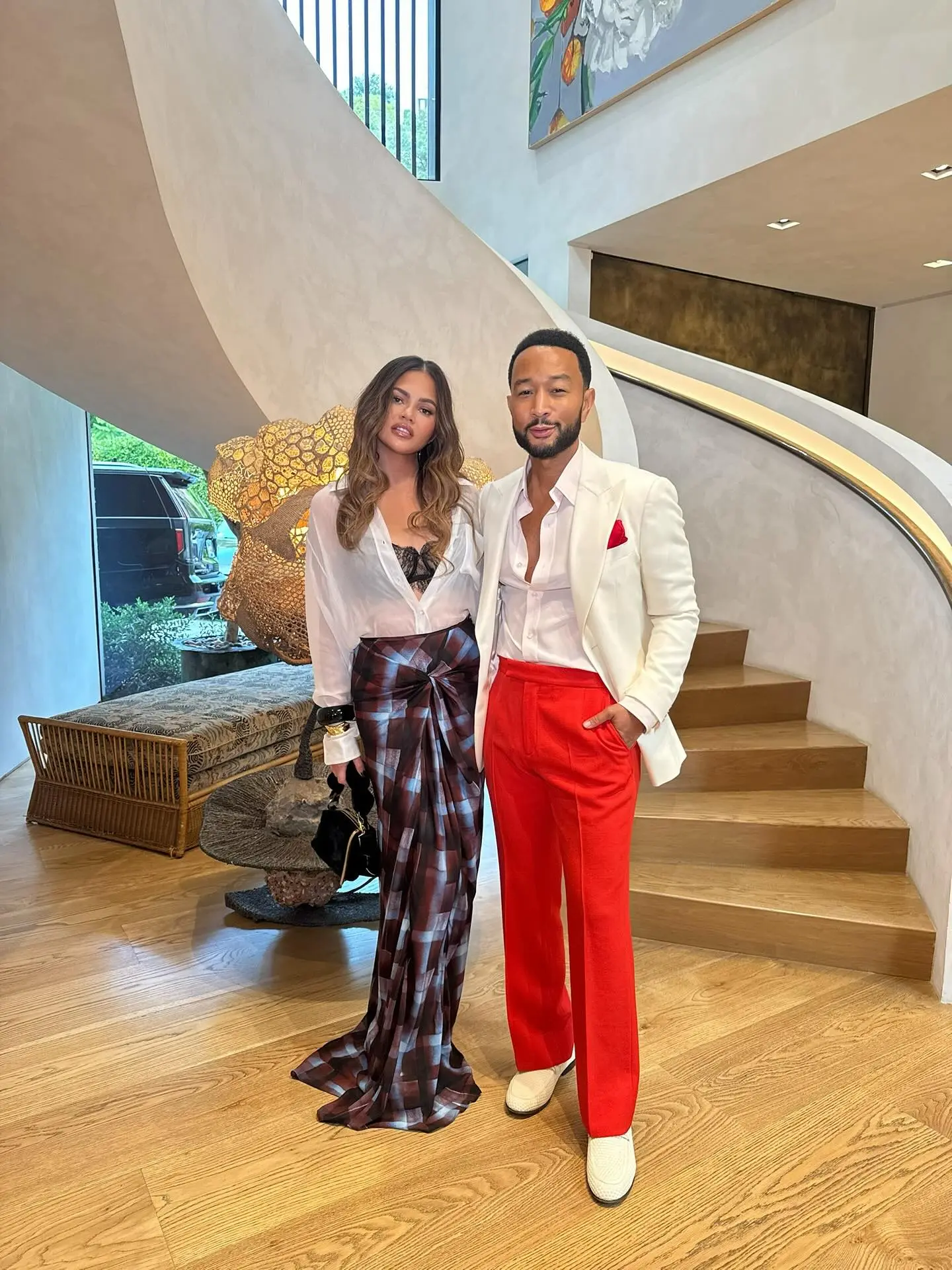 Chrissy Teigen and John Legend pose in a home with a curved staircase.