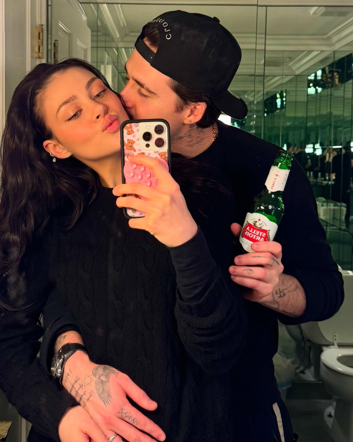 Brooklyn Beckham kissing Nicola Peltz on the cheek while she takes a mirror selfie.
