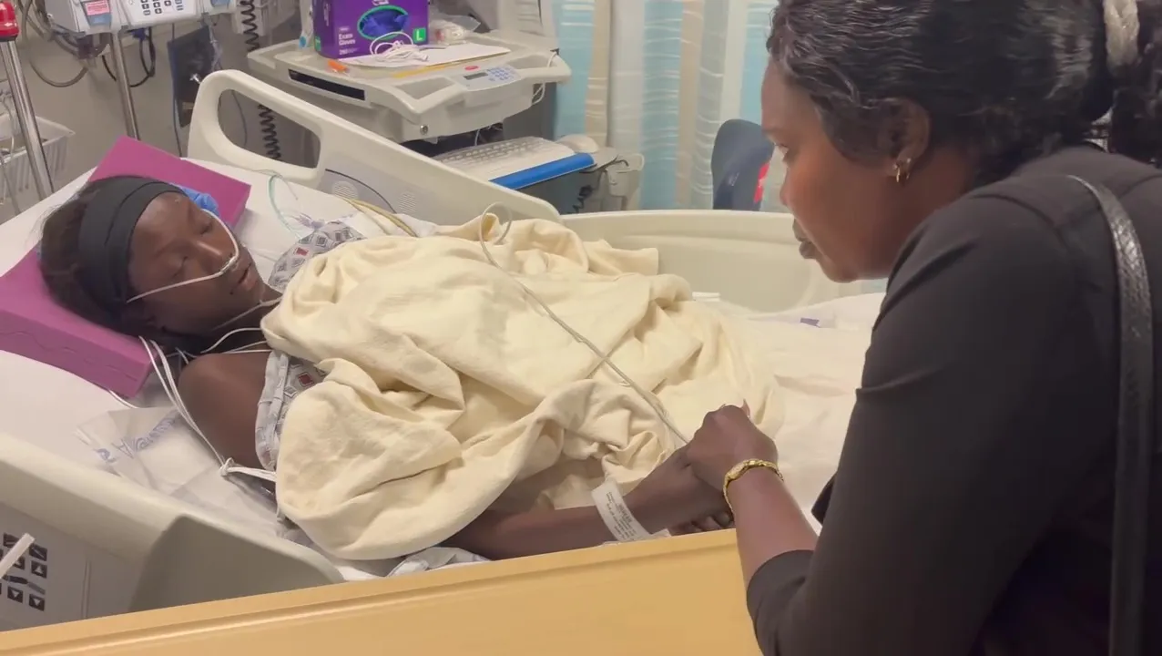 Anok Yai recovering in a hospital bed after robotic lung surgery, holding hands with a visitor.