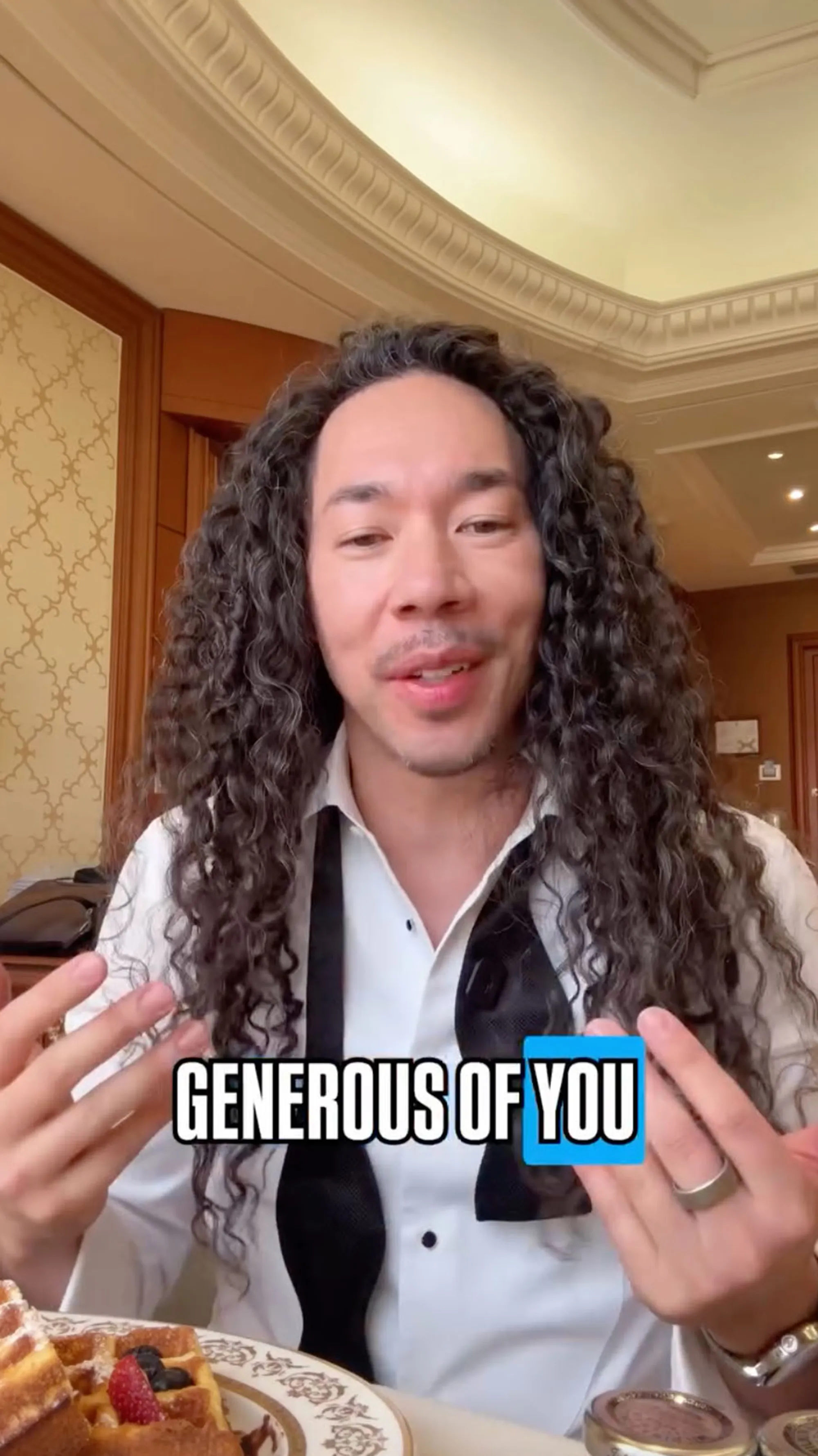 A man with long curly hair and a bow tie talking with his hands, with the words 