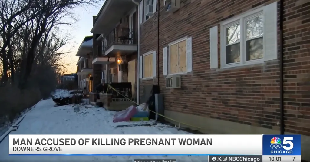Apartment complex with crime scene tape and boarded windows on a snowy day.