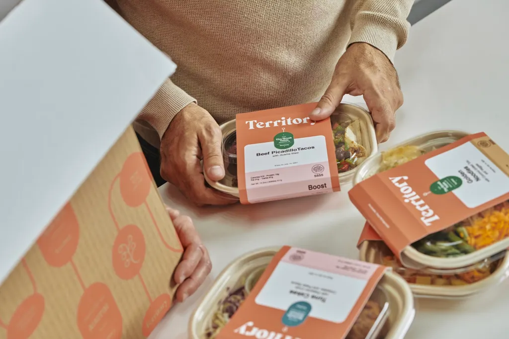 Person holding a Territory Foods meal container, with other containers visible on the table.