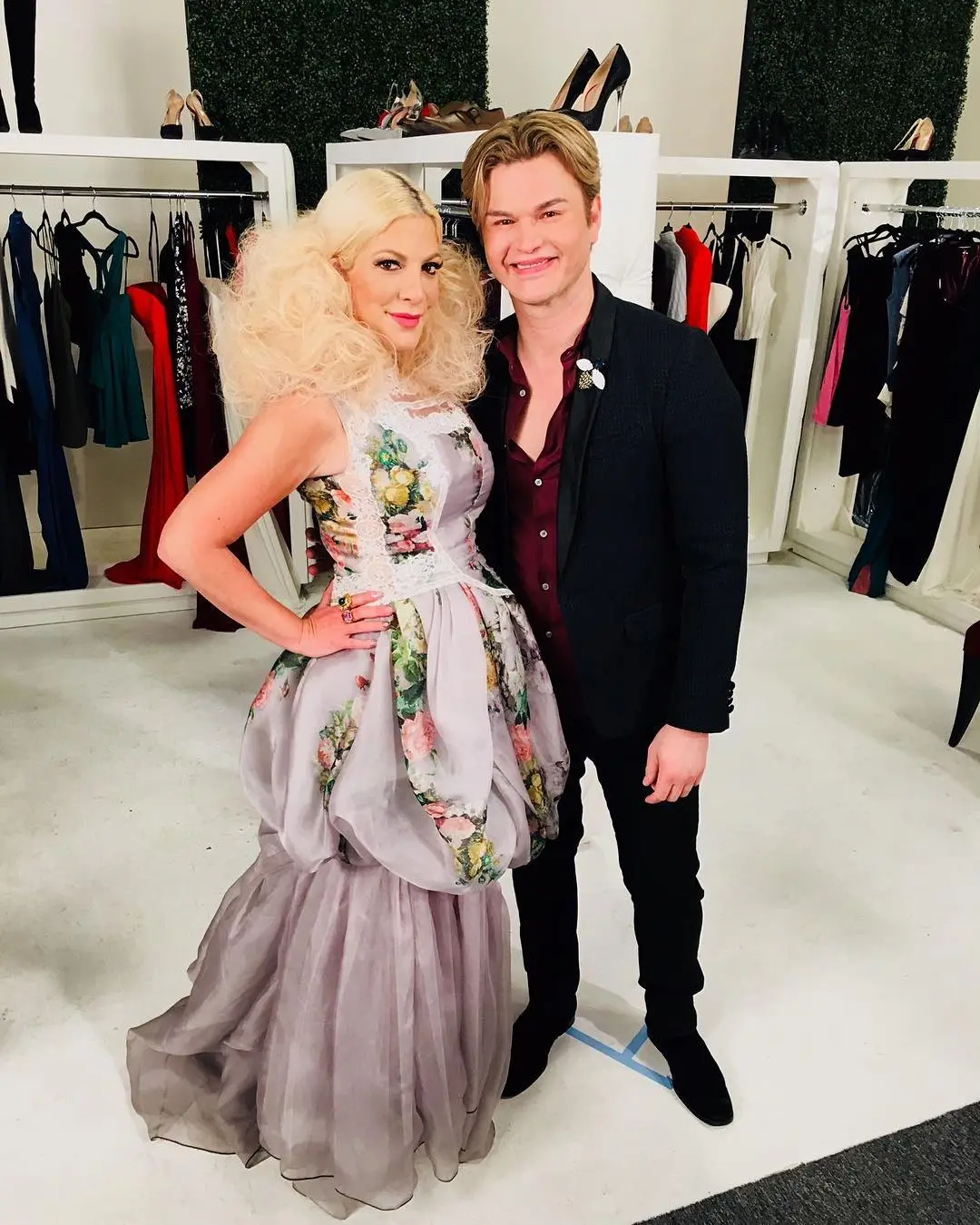 Tori Spelling with big blonde hair, wearing a floral gown next to Kim Vo.