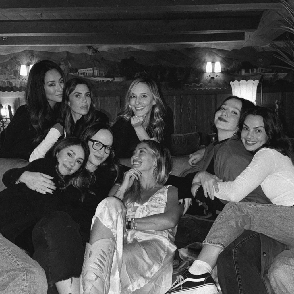 A black and white photo of eight women on a couch, some smiling at the camera, others looking at each other.