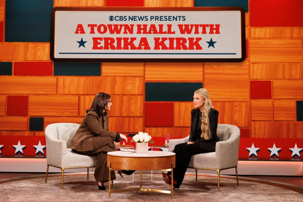 Erika Kirk, in black pant suit, and Bari Weiss, in a brown pant suit, sit in chairs on a stage in front of a screen that reads 