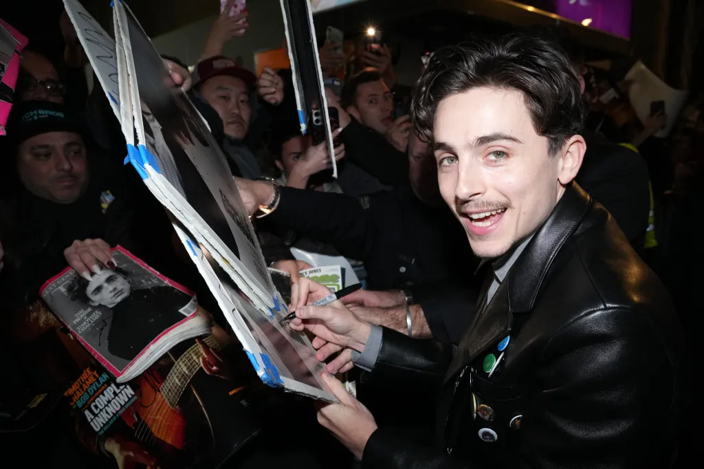 Timothée Chalamet smiling and signing autographs for fans at the premiere of