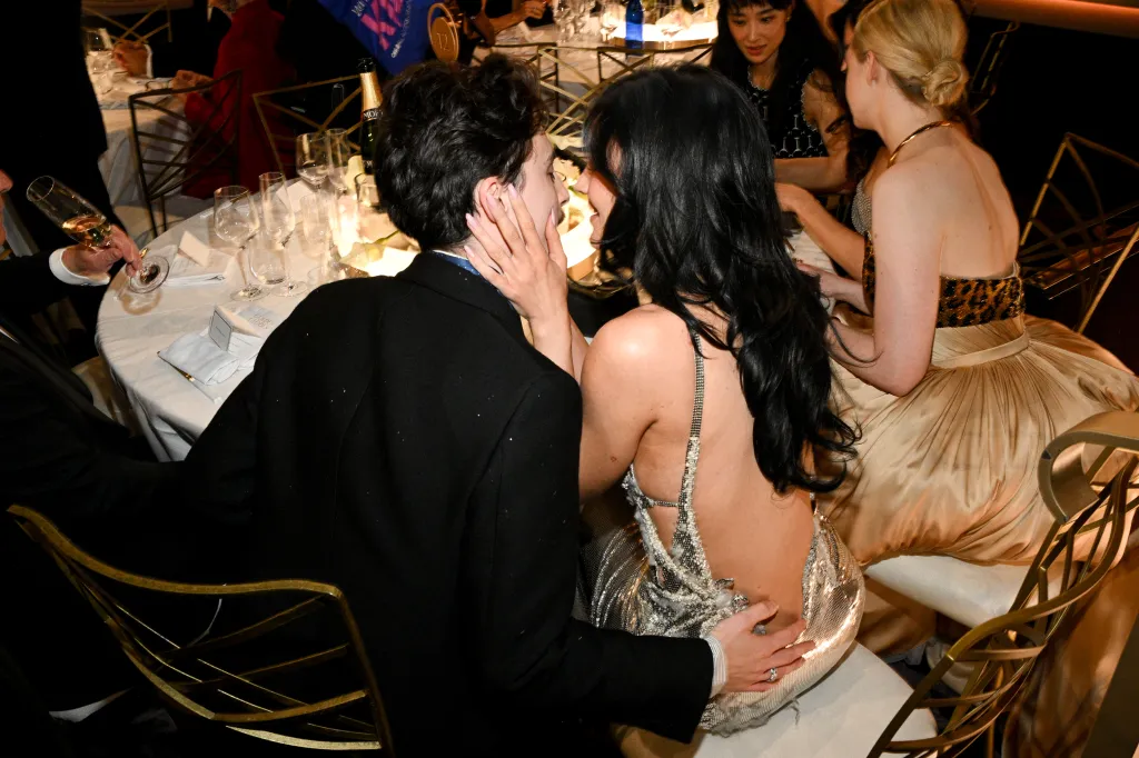 Timothée Chalamet and Kylie Jenner seated at a table, with Jenner's arm around Chalamet and his hand on her waist.